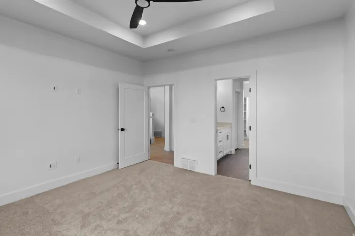 Unfurnished bedroom featuring a raised ceiling, light carpet, ceiling fan, connected bathroom, and recessed lighting