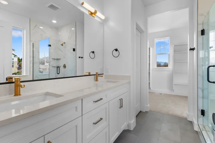 Bathroom featuring double vanity, a marble finish shower, and dark tile patterned flooring