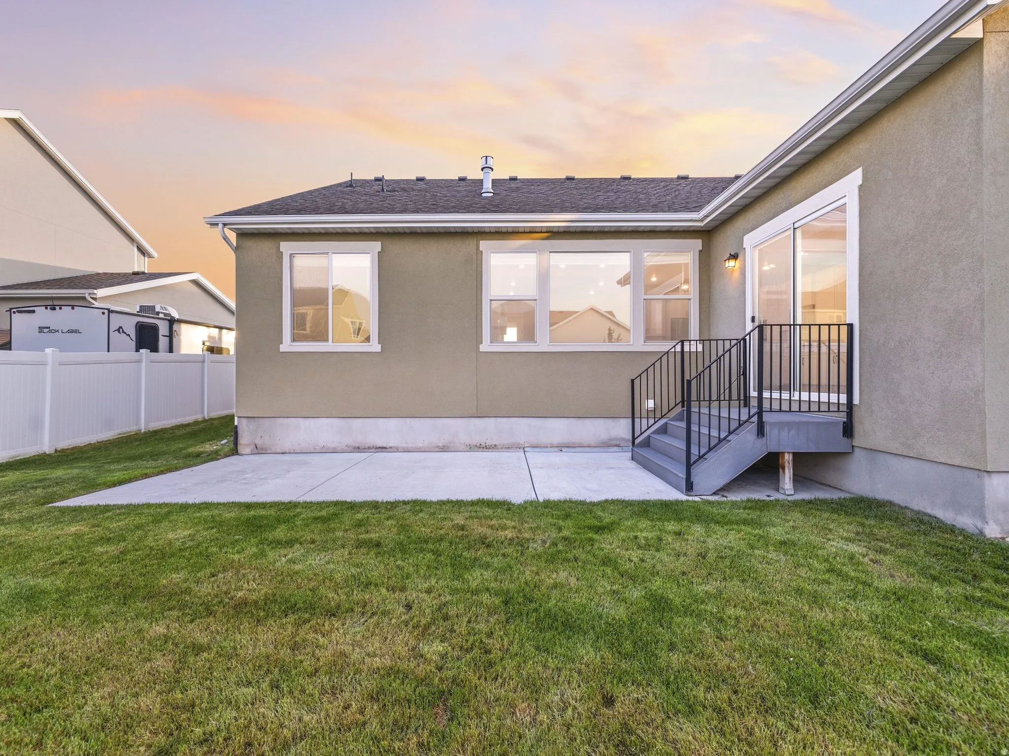 Back of house at dusk with stucco siding, a patio area, and roof with shingles