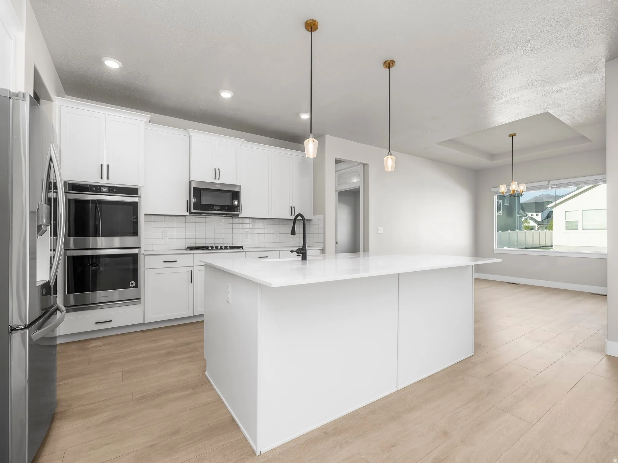 Kitchen with light wood-style flooring, stainless steel appliances, backsplash, white cabinetry, and a raised ceiling