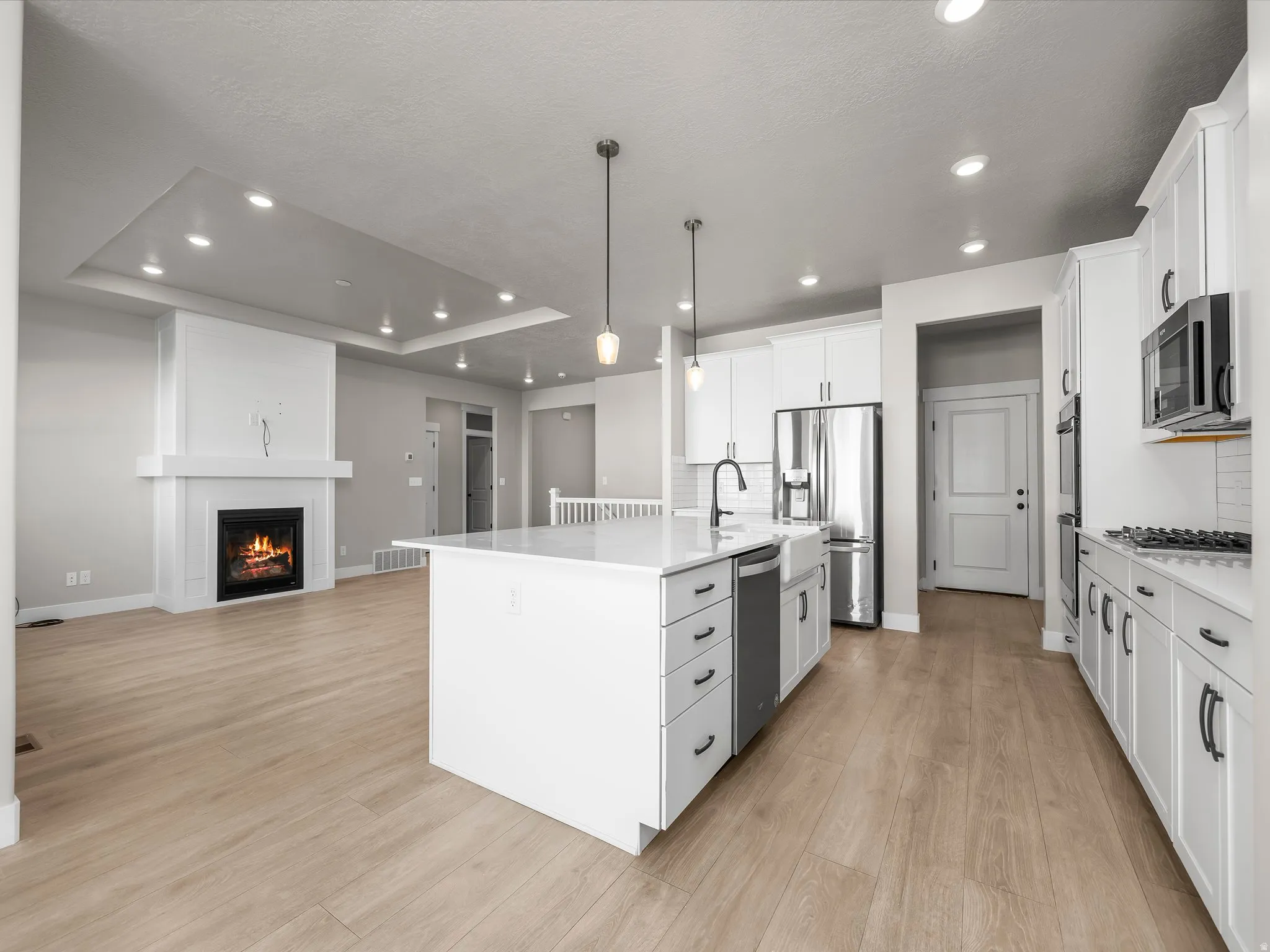 Kitchen with white cabinetry, a kitchen island with sink, a glass covered fireplace, stainless steel appliances, and a tray ceiling