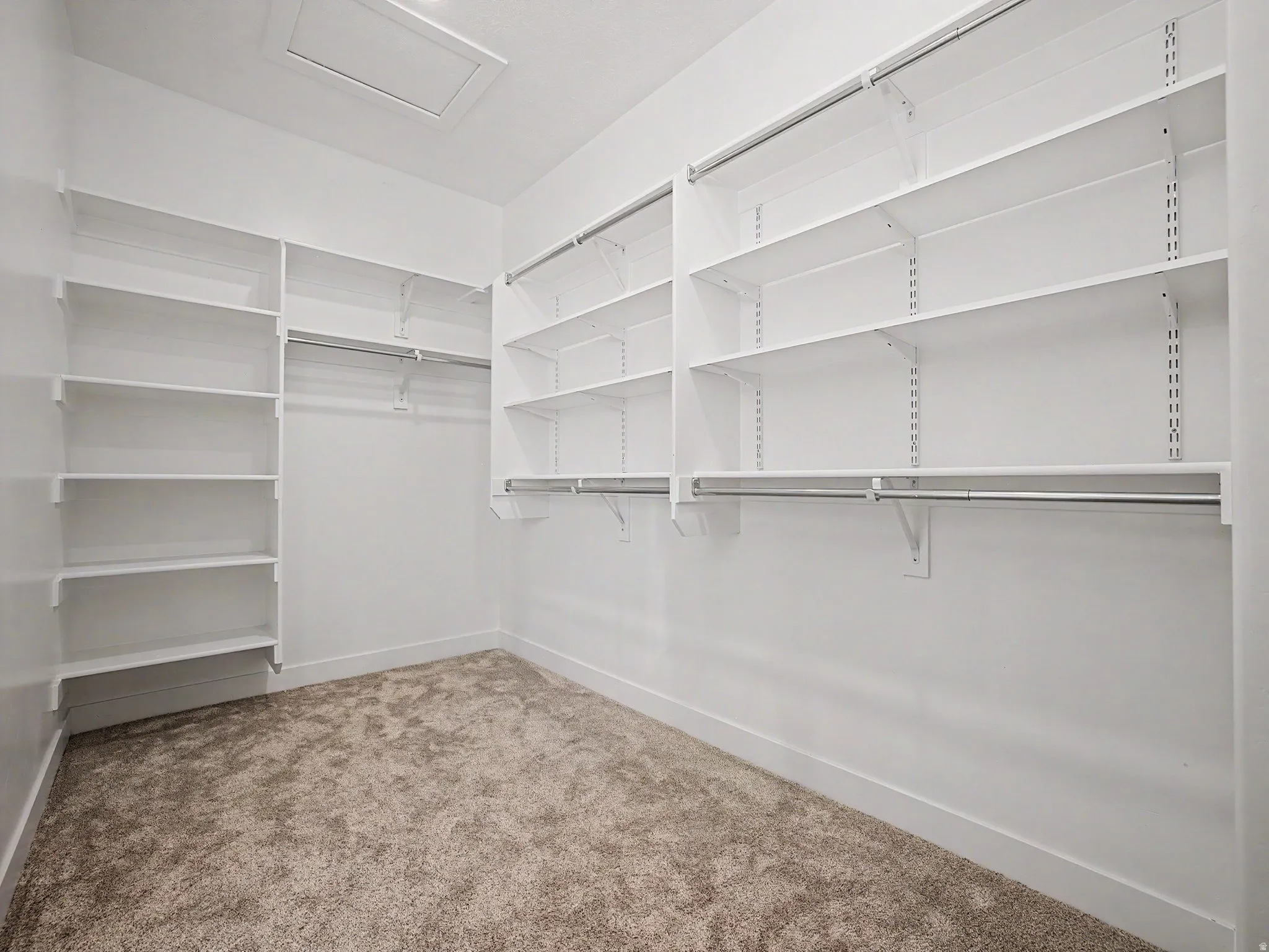 Walk in closet with light carpet and attic access