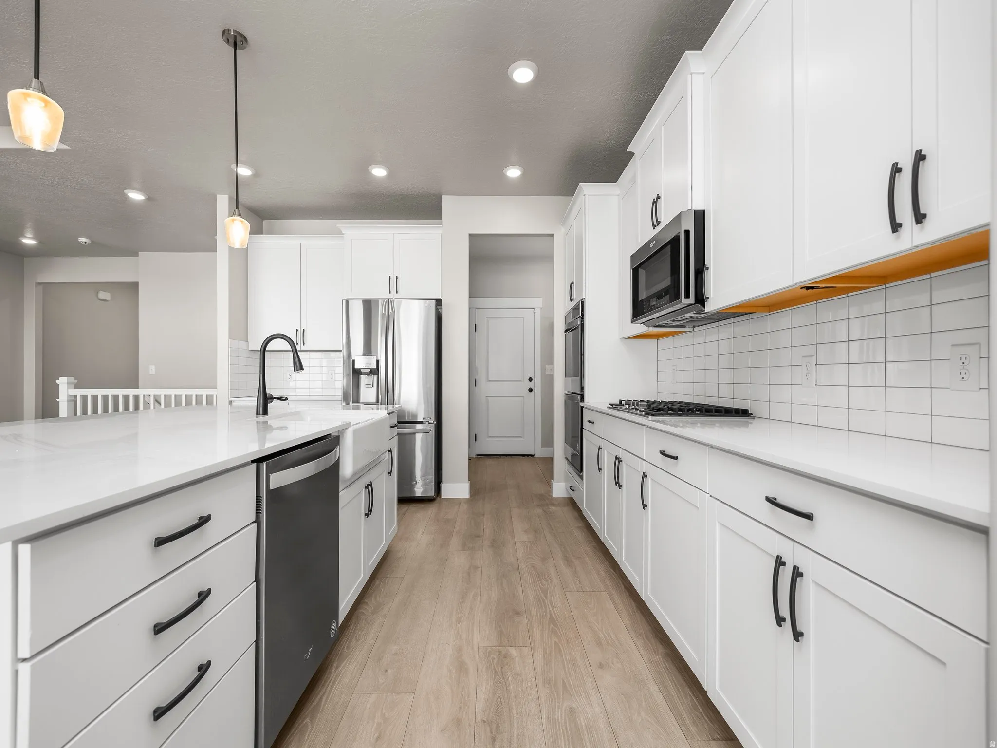 Kitchen featuring light stone countertops, stainless steel appliances, light wood finished floors, white cabinets, and hanging light fixtures