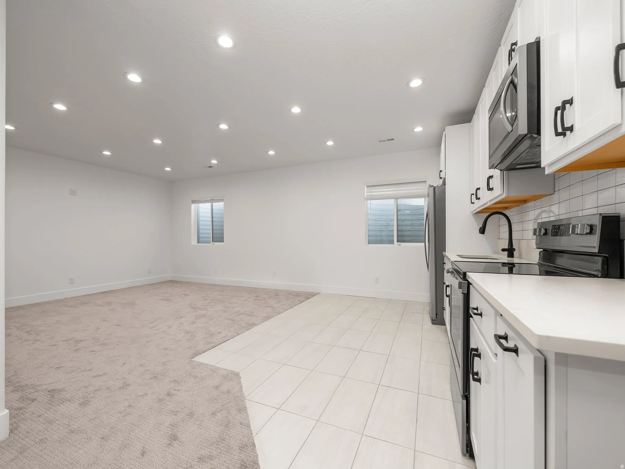 Kitchen with stainless steel appliances, light colored carpet, white cabinets, tasteful backsplash, and light tile patterned floors