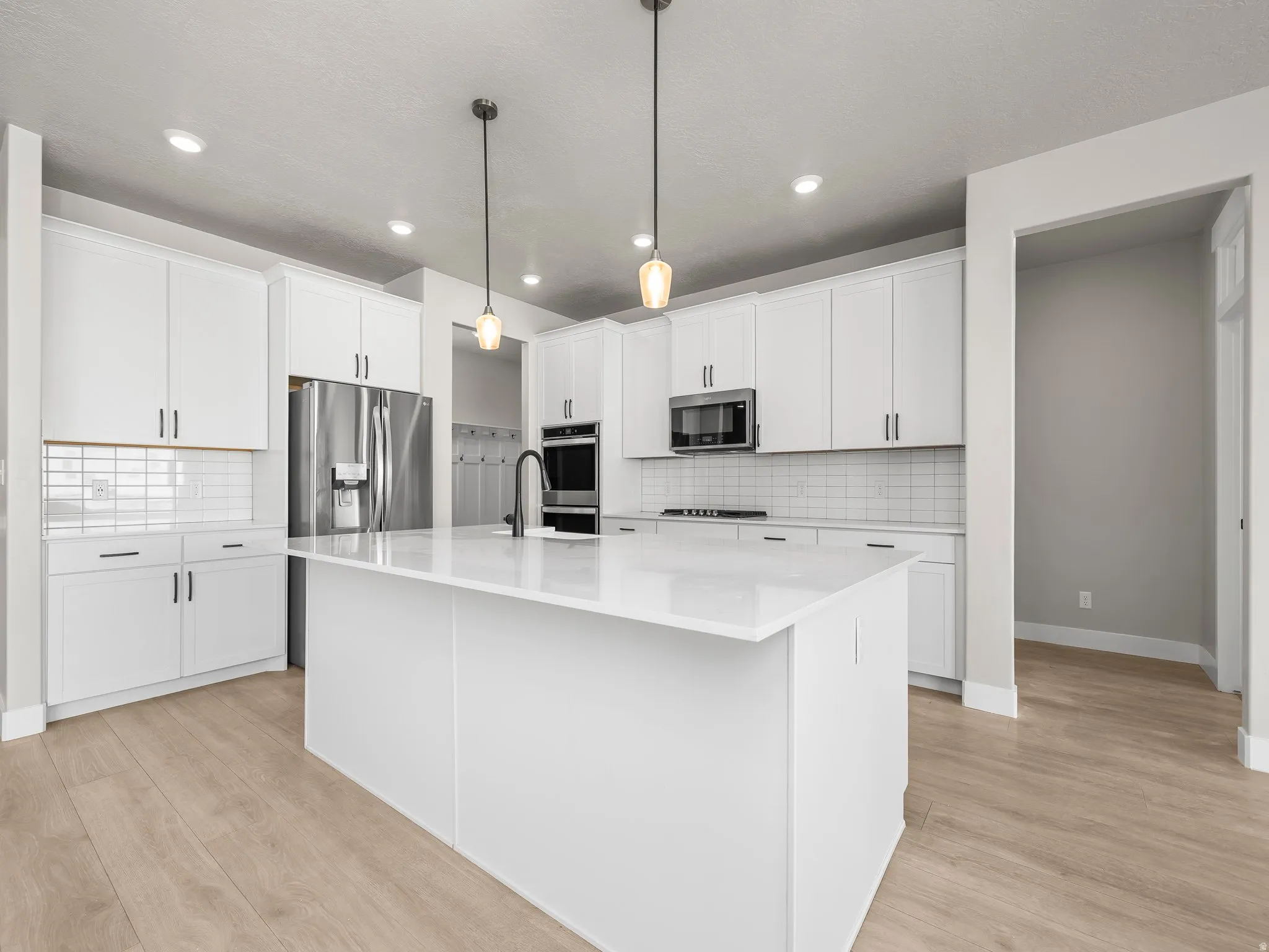 Kitchen with white cabinetry, a center island with sink, hanging light fixtures, and light wood finished floors