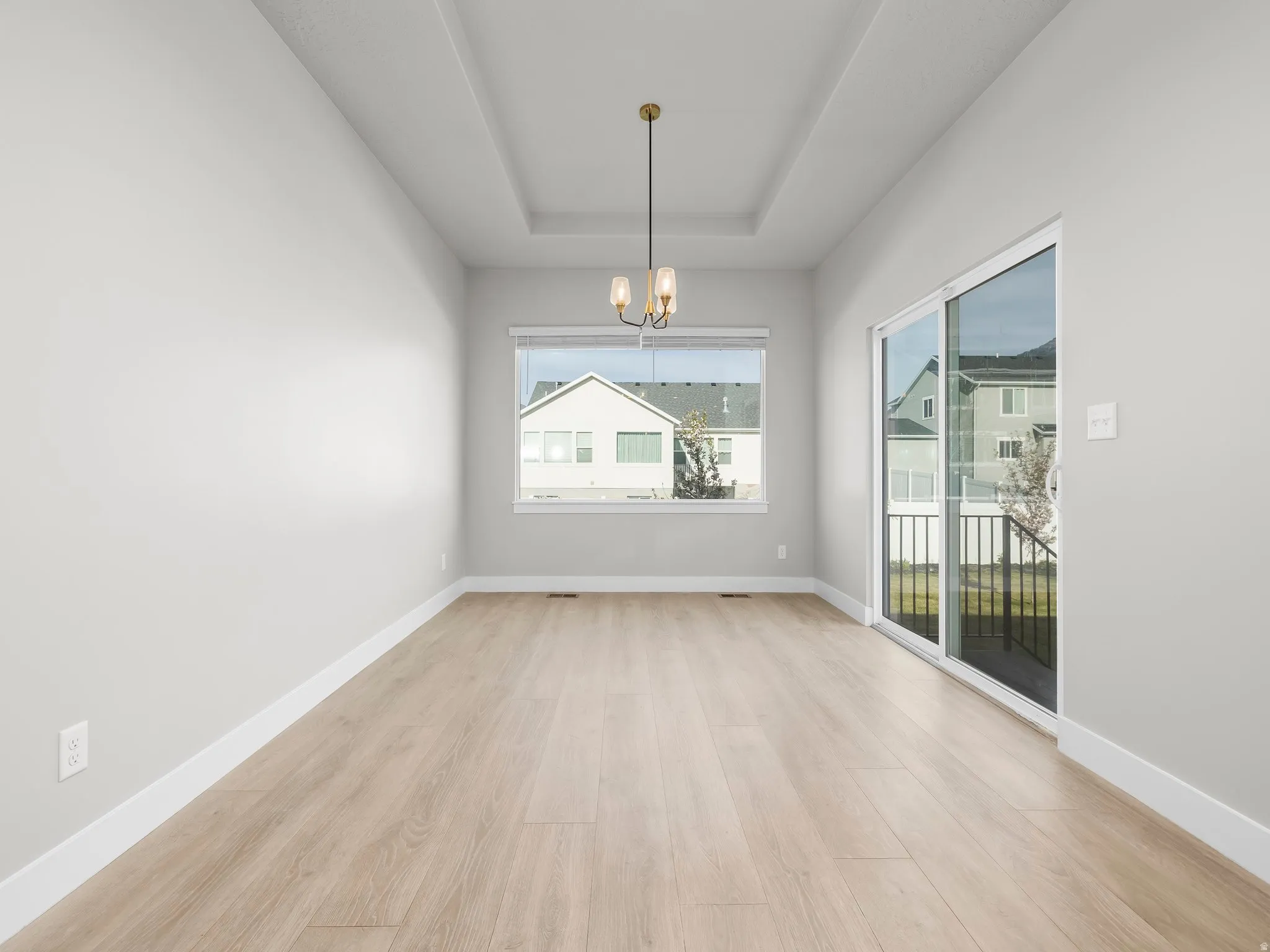 Unfurnished dining area featuring suspended lighting, light wood-type flooring, and a tray ceiling