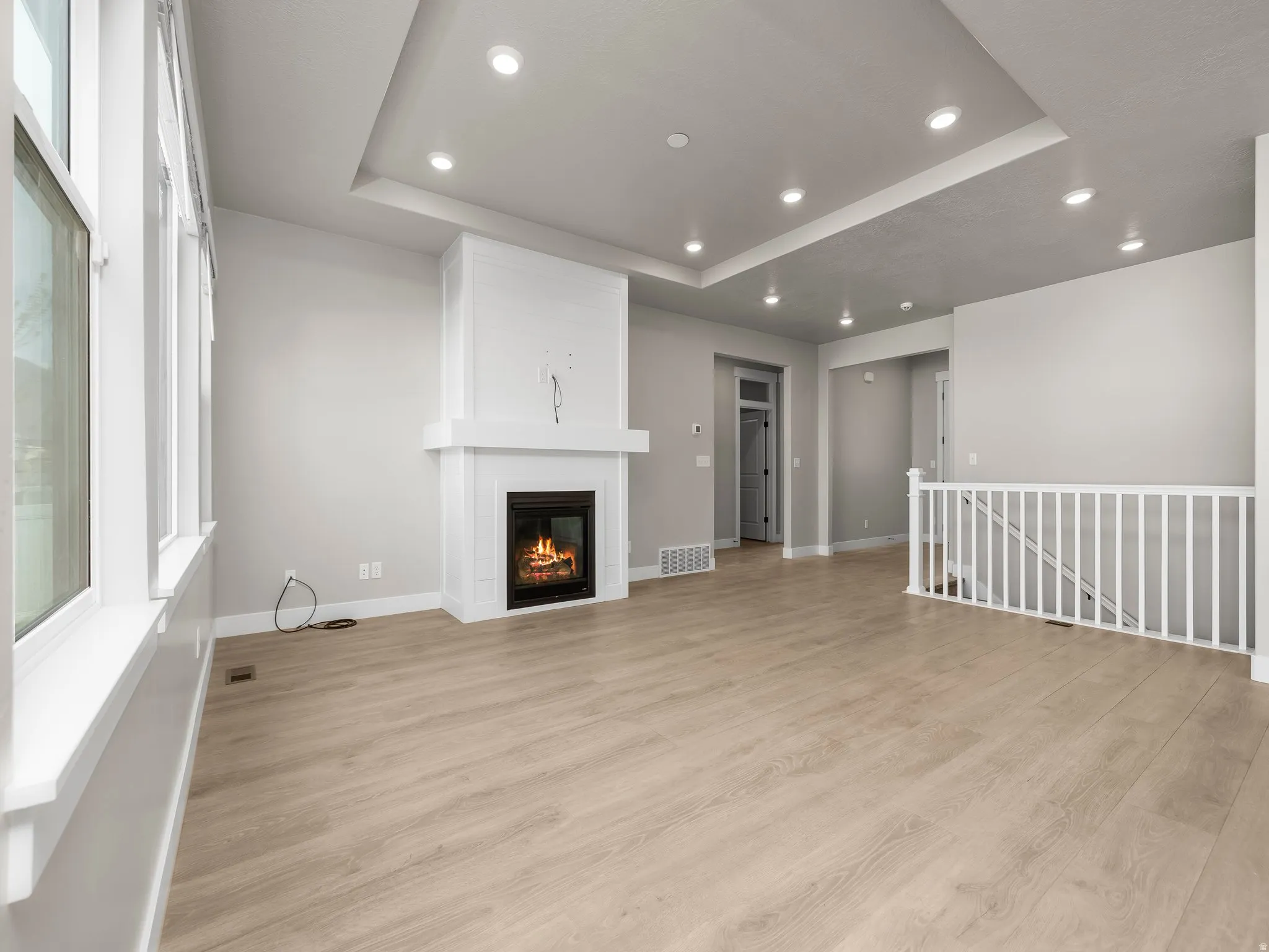 Unfurnished living room featuring a raised ceiling, recessed lighting, light wood-style flooring, and a large fireplace