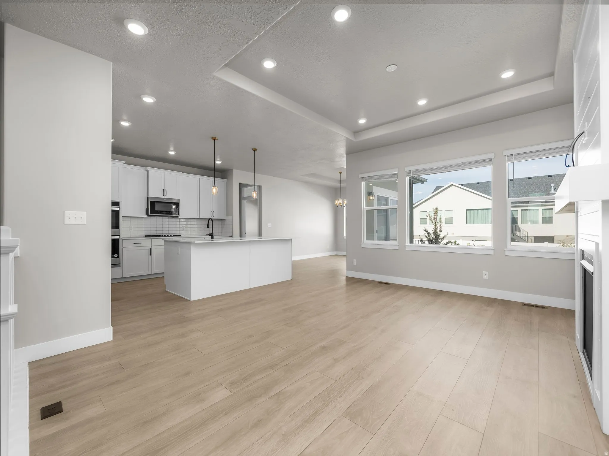 Kitchen featuring pendant lighting, open floor plan, white cabinets, decorative backsplash, and an island with sink