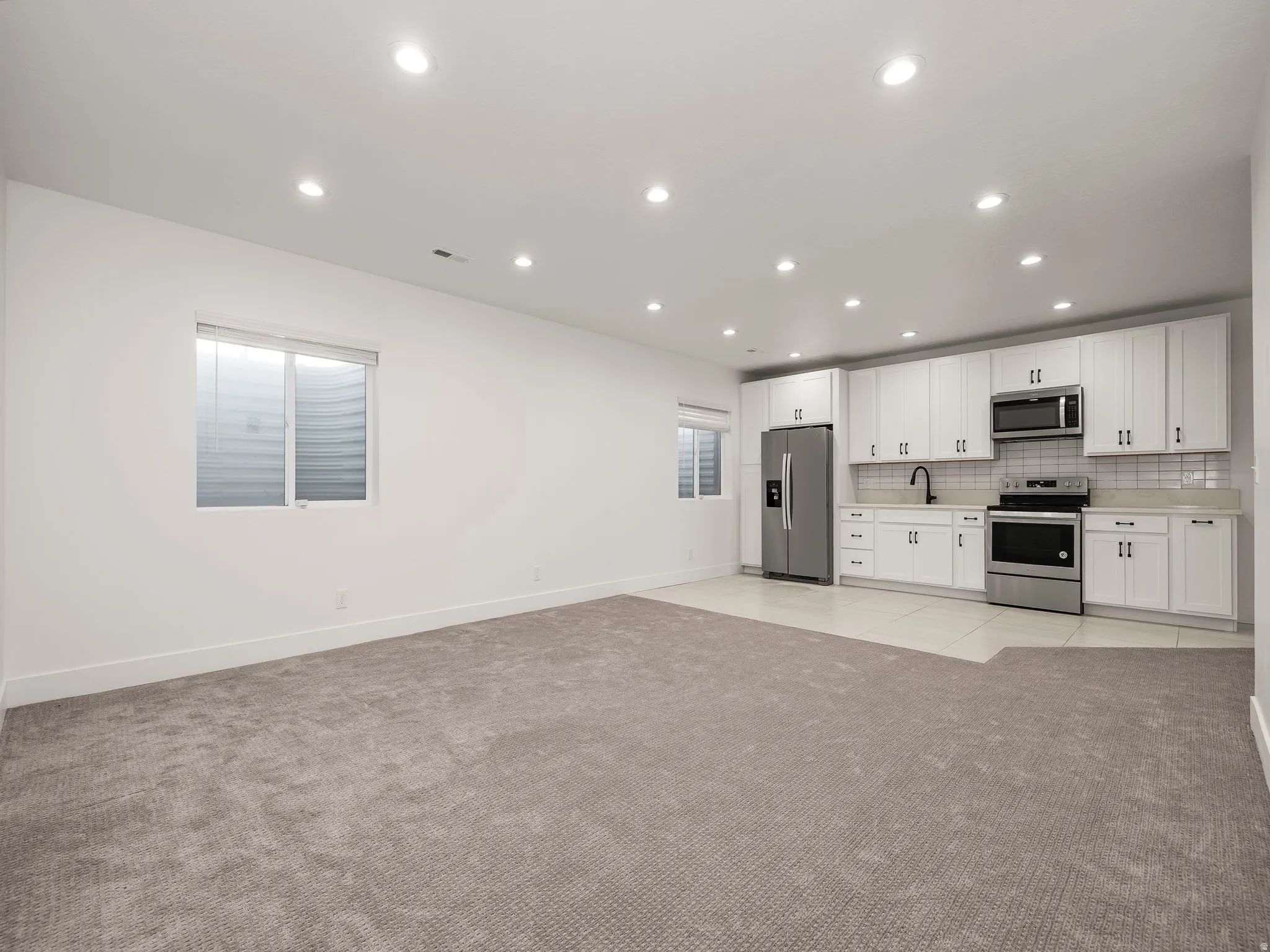 Kitchen with stainless steel appliances, recessed lighting, white cabinets, open floor plan, and light colored carpet