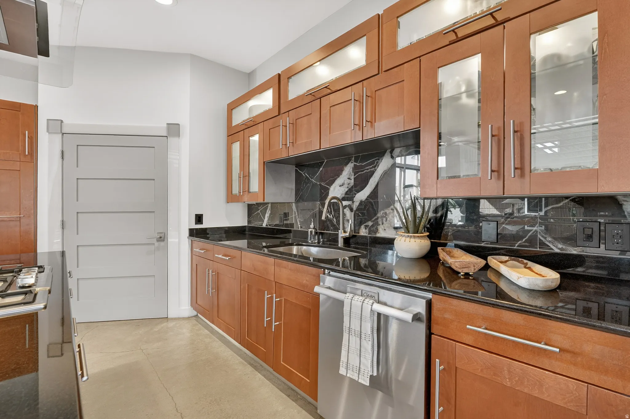 Kitchen featuring wood finish cabinetry, dark stone countertops, decorative backsplash, concrete flooring, and recessed lighting