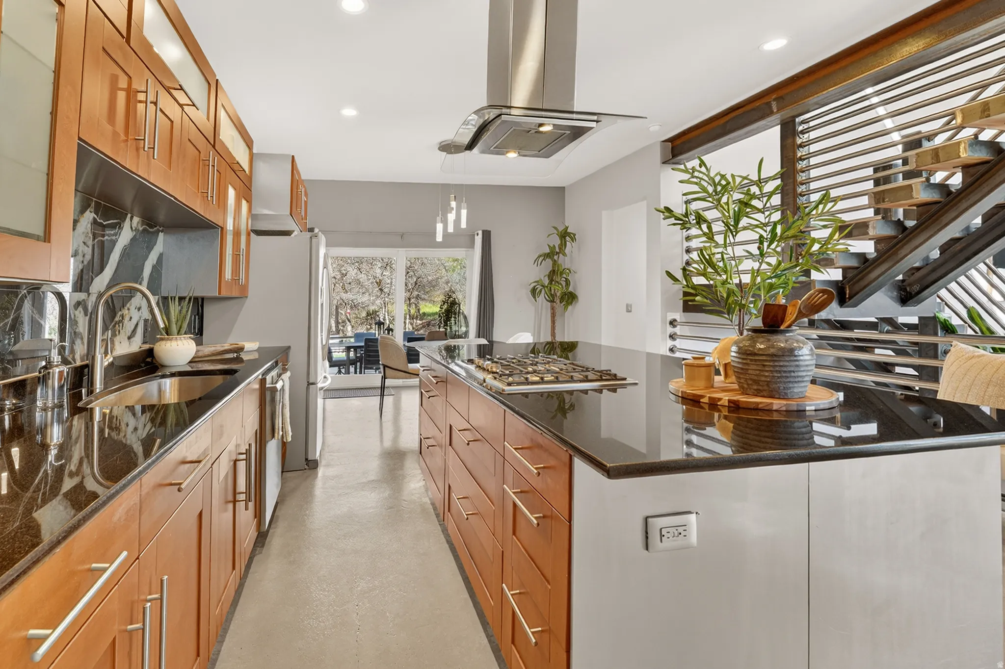 Kitchen with dark stone counters, a large island, glass fronted cabinets, island range hood, and finished concrete flooring