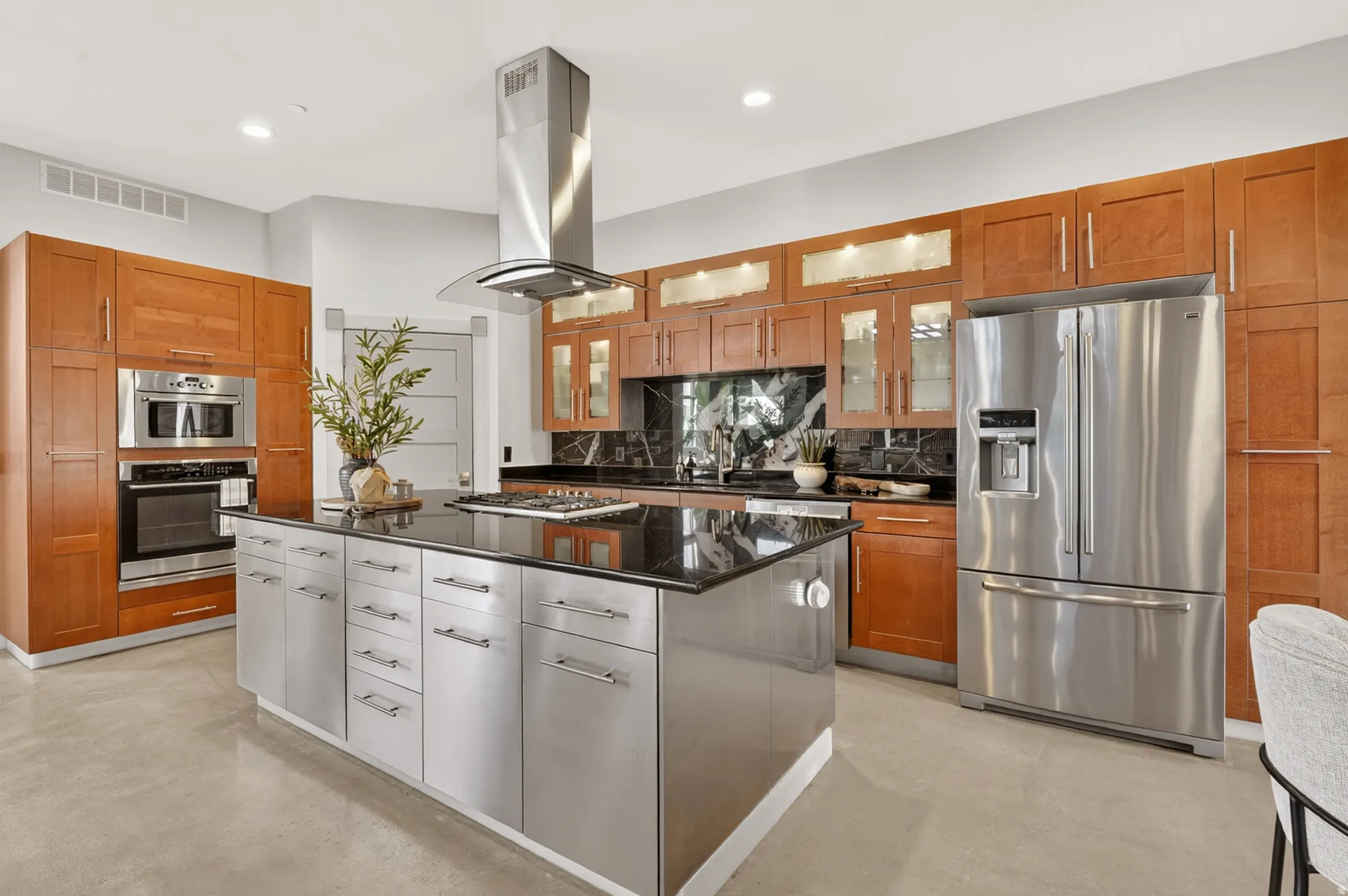 Dual tone kitchen with stainless steel appliances, glass insert cabinets, dark stone counters, a center island, and concrete flooring