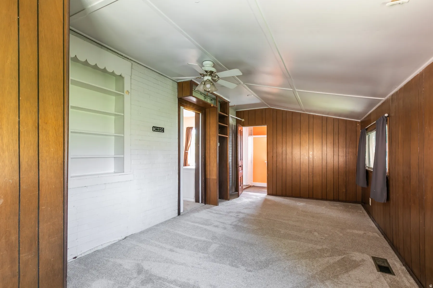 Unfurnished room with light carpet, wood walls, lofted ceiling, a ceiling fan, and built in features