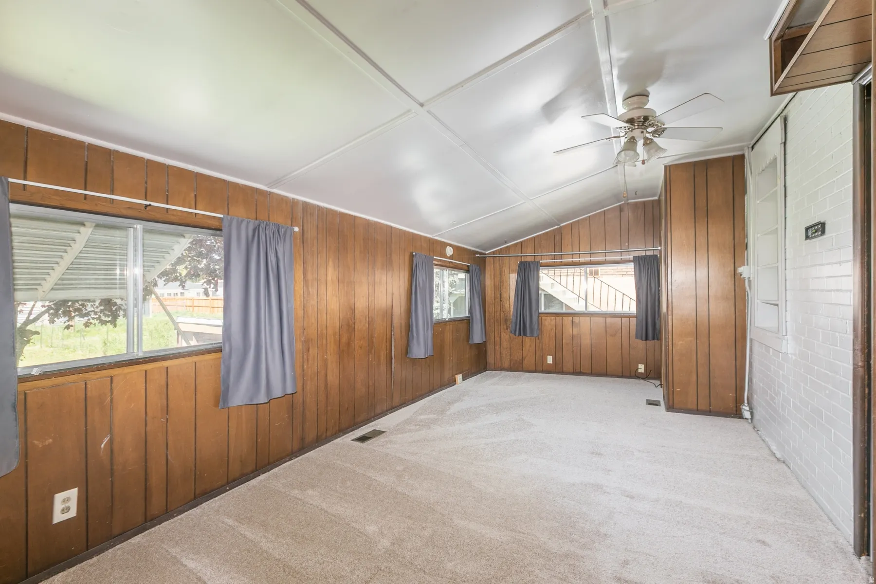 Spare room with lofted ceiling, light colored carpet, ceiling fan, and wooden walls