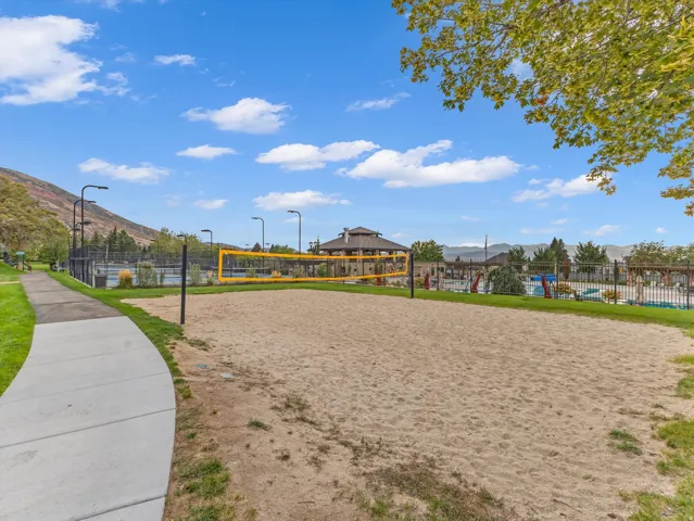 Sand volleyball court with a yellow net, bordered by green grass and a concrete pathway