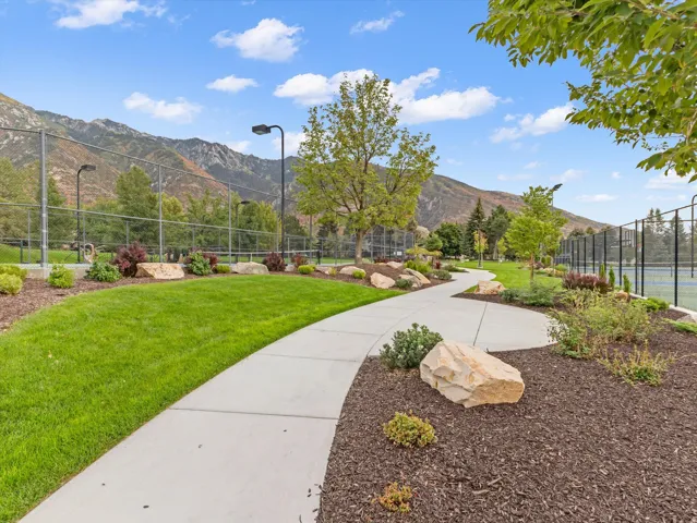 Winding paved pathway through landscaped grounds, featuring mature trees, ornamental shrubs, and decorative boulders