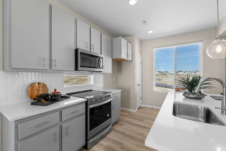 Kitchen featuring gray cabinetry, stainless steel appliances, light wood-style floors, decorative light fixtures, and backsplash