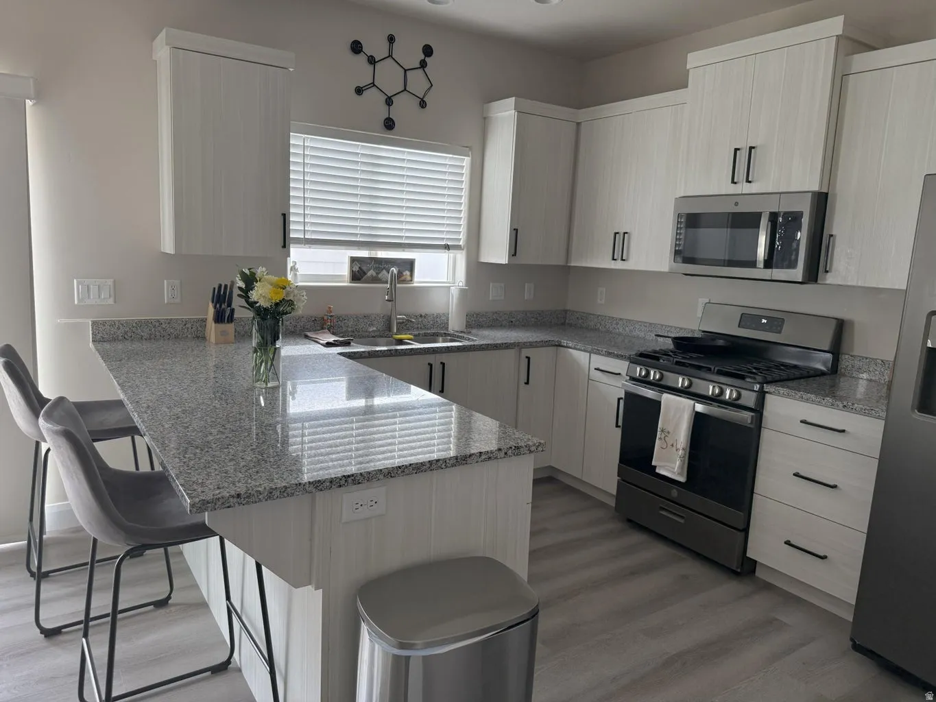 Kitchen featuring a breakfast bar, stainless steel appliances, a peninsula, light stone countertops, and light wood finished floors