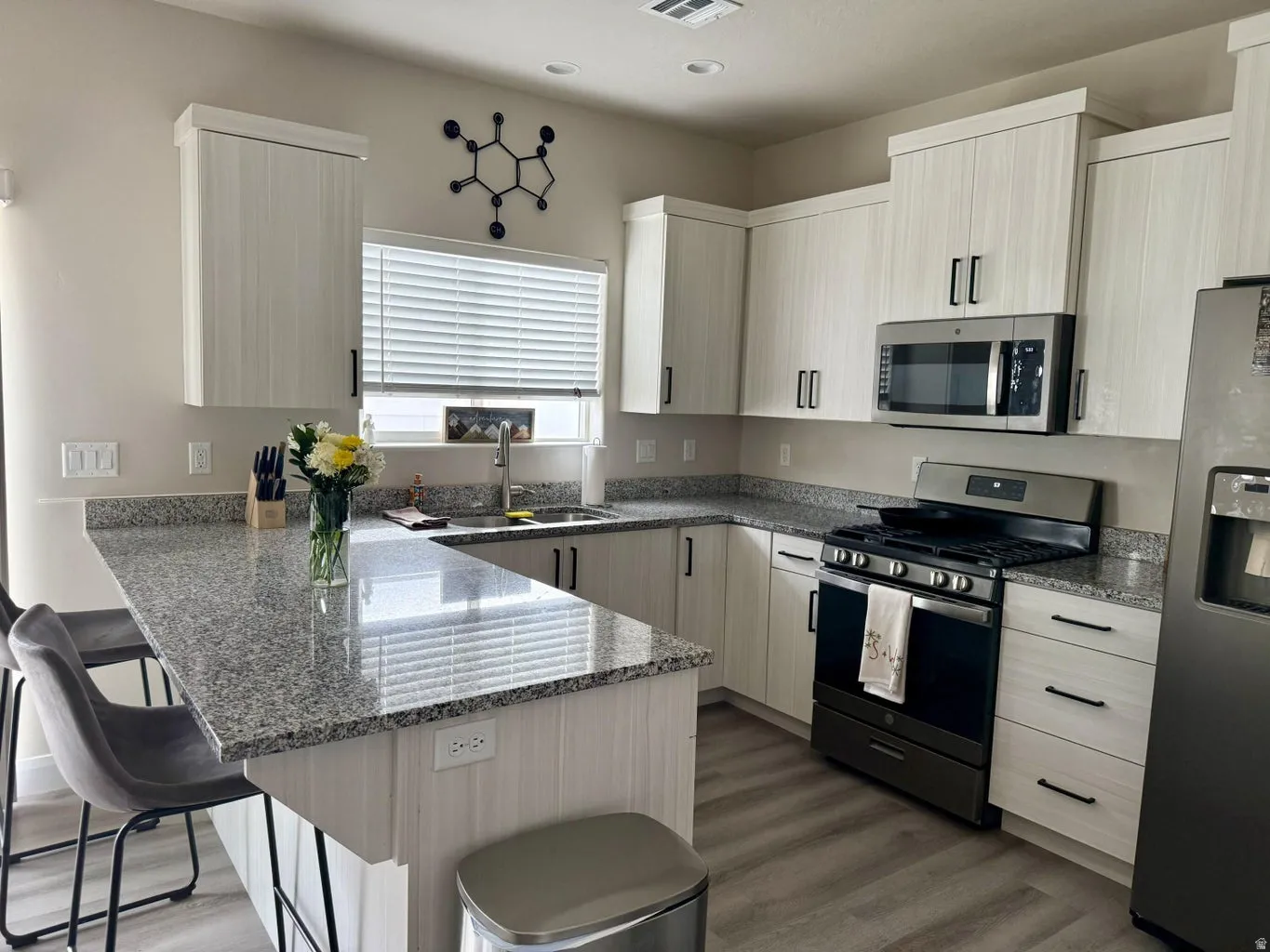 Kitchen with a breakfast bar area, a peninsula, stainless steel appliances, light stone countertops, and dark wood-style floors