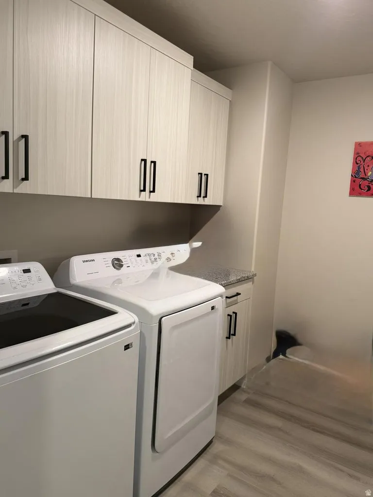 Laundry room featuring light wood-style floors, cabinet space, and washing machine and clothes dryer