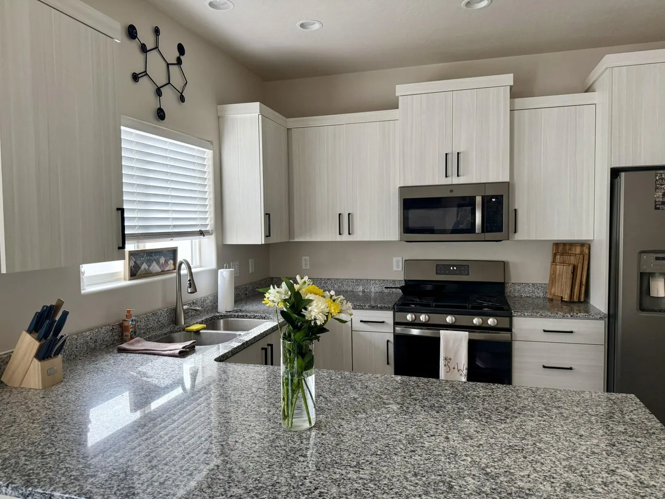 Kitchen with light stone counters, stainless steel appliances, a peninsula, modern cabinets, and recessed lighting