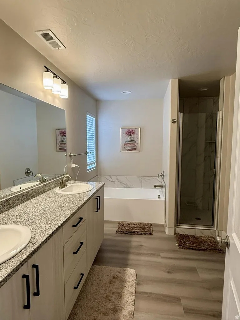Full bath featuring double vanity, a bath, a marble finish shower, light wood-type flooring, and a textured ceiling