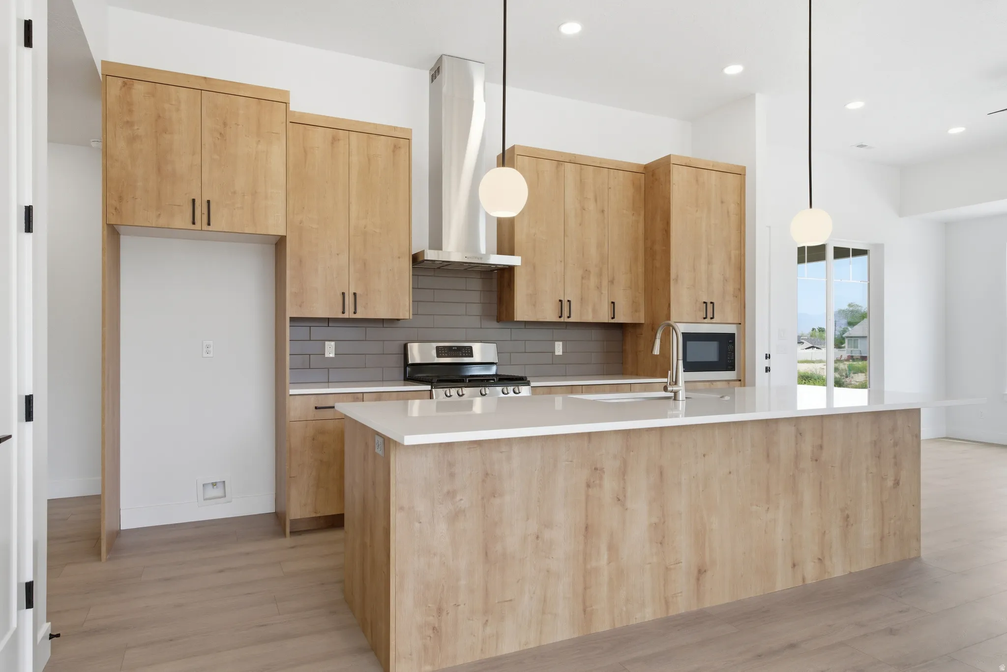 Kitchen featuring light wood finish cabinetry, a kitchen island with sink, decorative light fixtures, and light wood-type flooring