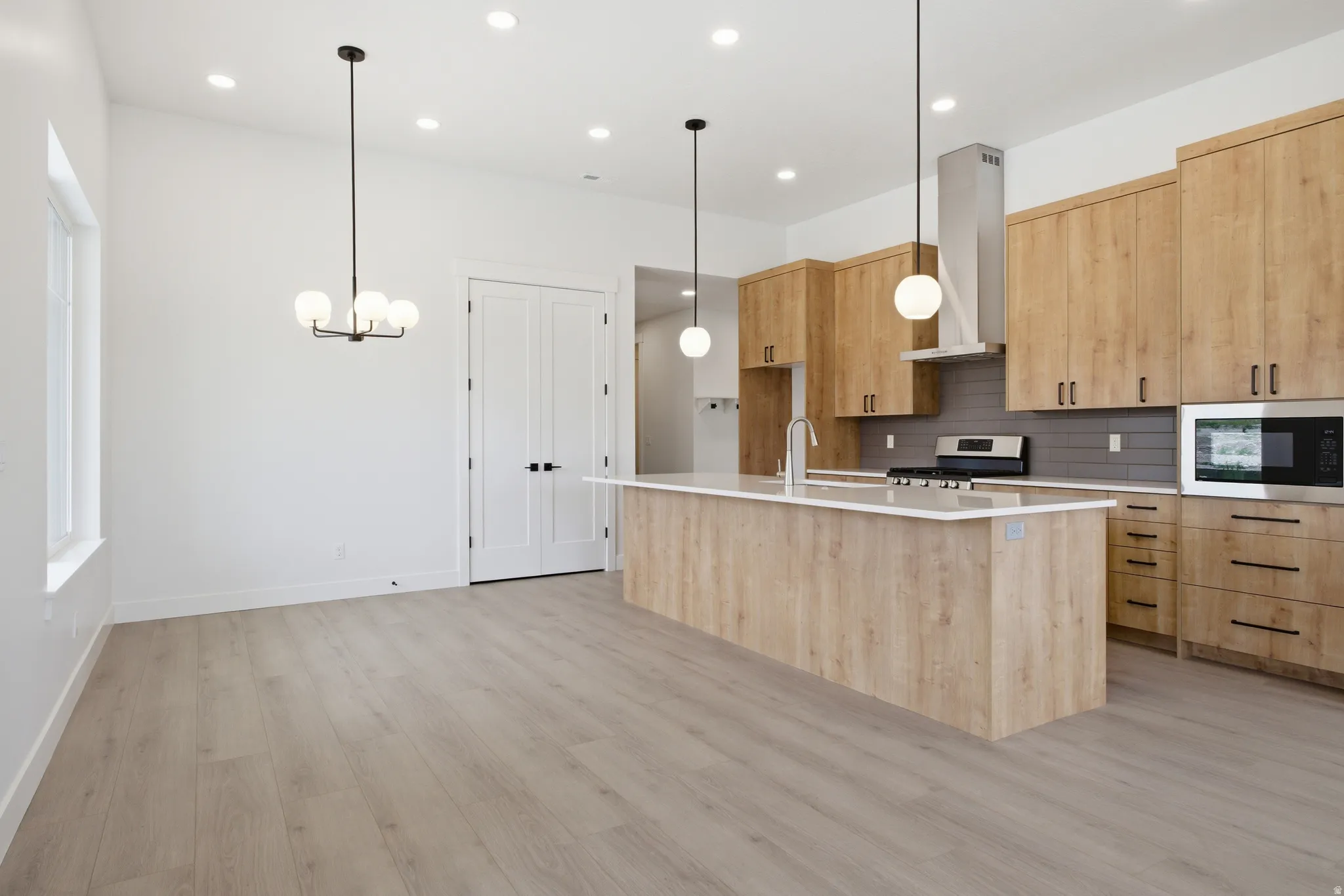 Kitchen featuring light wood finish cabinetry, a center island with sink, light wood-style flooring, hanging lights, and modern cabinets