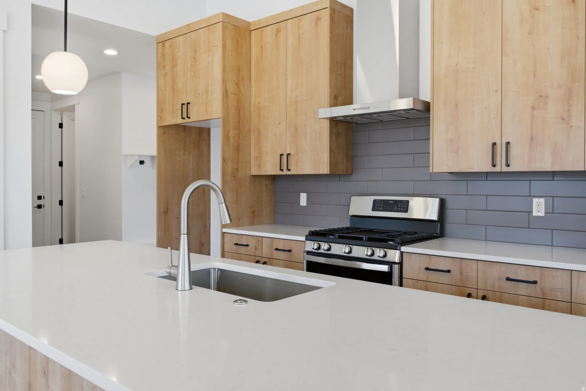 Kitchen featuring light wood finish cabinetry, stainless steel range with gas cooktop, light stone countertops, backsplash, and recessed lighting