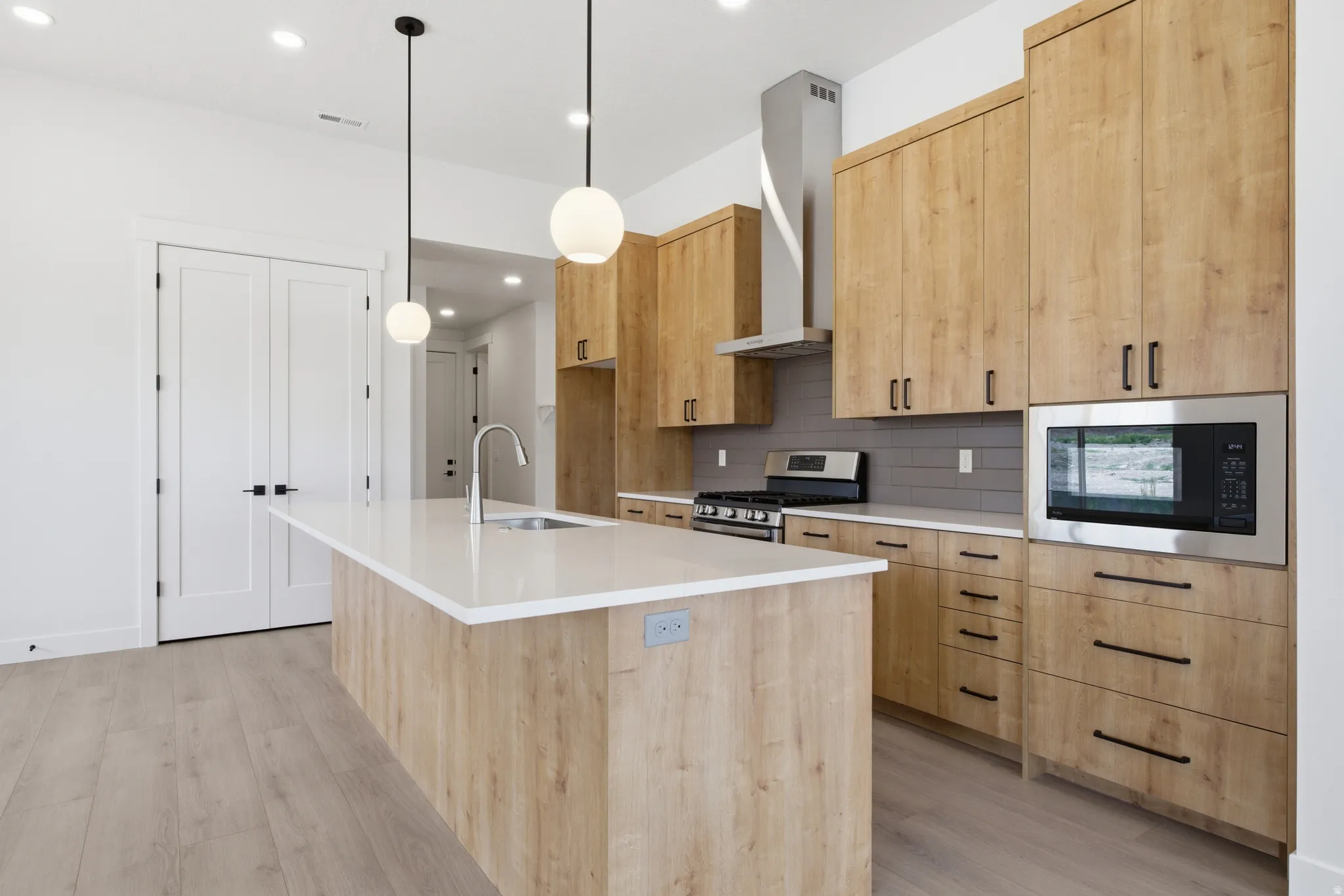 Kitchen featuring light wood finish cabinetry, a kitchen island with sink, tasteful backsplash, and stainless steel gas range