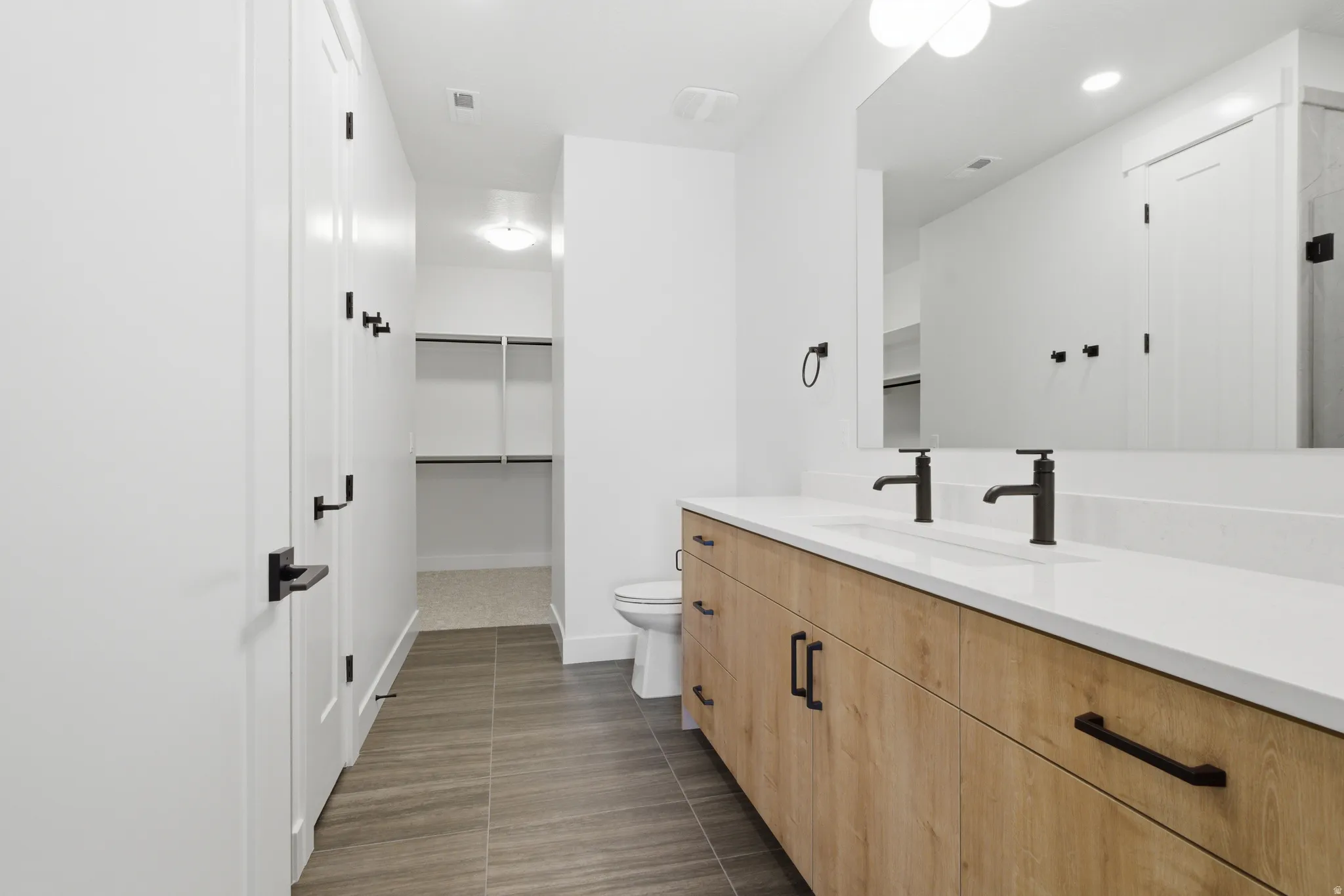 Full bathroom with vanity, a walk in closet, and dark tile patterned flooring