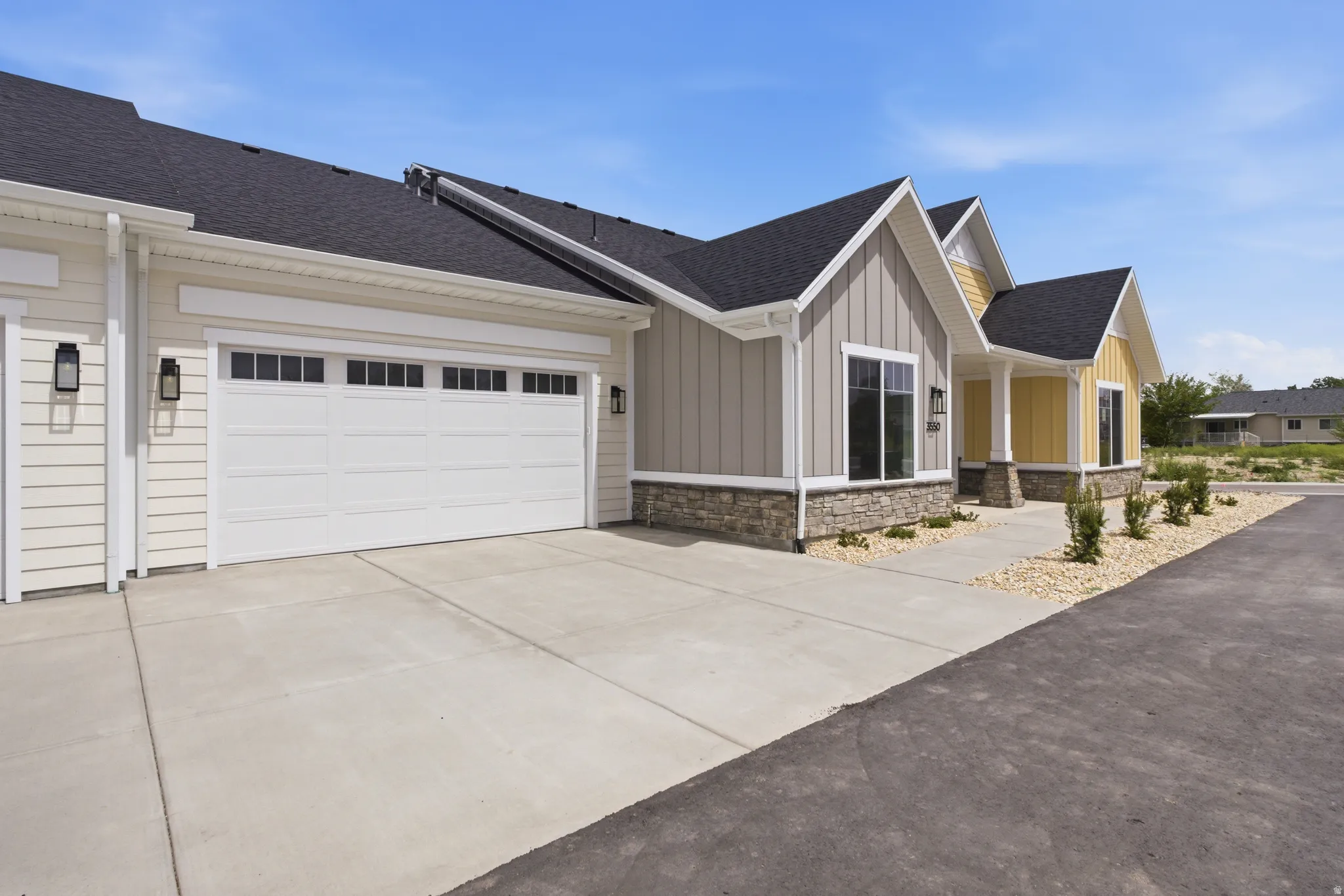 View of front facade featuring roof with shingles, board and batten siding, concrete driveway, stone siding, and a garage