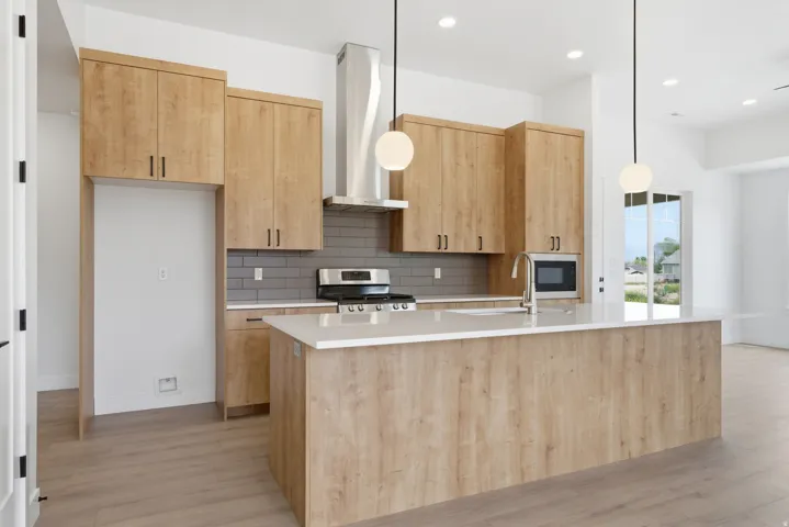 Kitchen featuring light wood finish cabinetry, a kitchen island with sink, decorative light fixtures, and light wood-type flooring