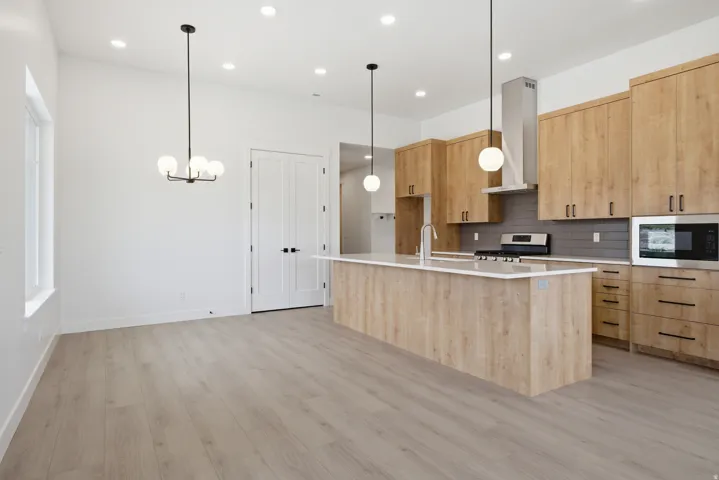 Kitchen featuring light wood finish cabinetry, a center island with sink, light wood-style flooring, hanging lights, and modern cabinets