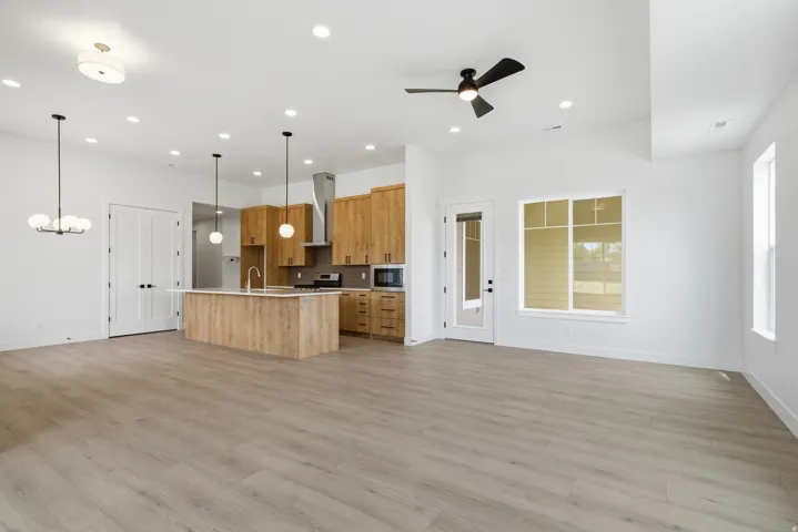 Kitchen with open floor plan, a kitchen island with sink, a ceiling fan, hanging light fixtures, and light wood-type flooring