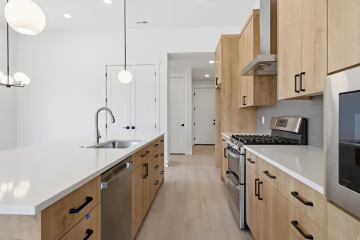 Kitchen featuring light wood finish cabinets, stainless steel appliances, light wood-type flooring, light stone counters, and a kitchen island with sink