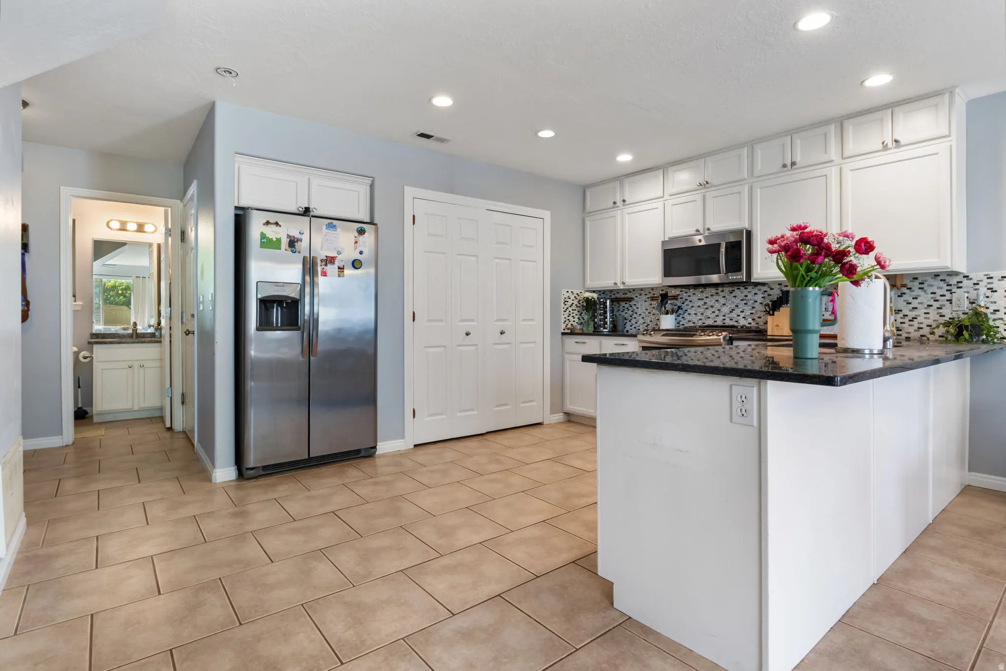 Kitchen featuring stainless steel appliances, a peninsula, white cabinetry, dark stone counters, and backsplash