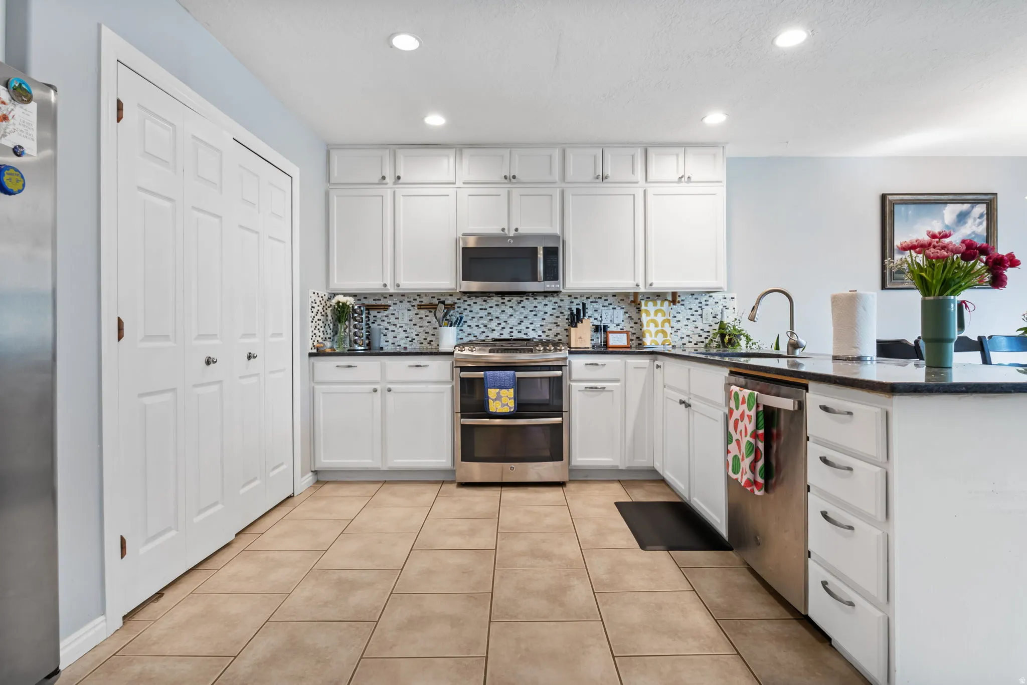 Kitchen with white cabinets, stainless steel appliances, a peninsula, recessed lighting, and backsplash