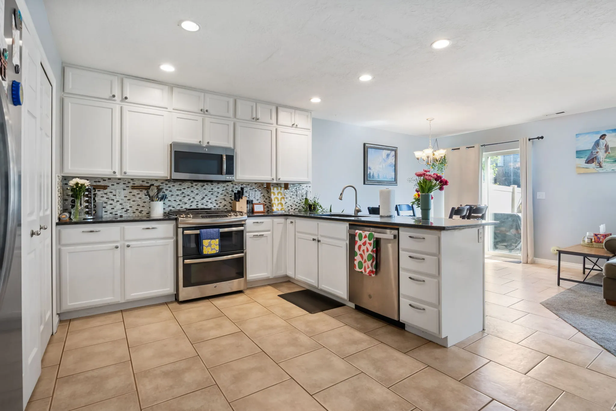 Kitchen with dark countertops, white cabinetry, a peninsula, stainless steel appliances, and tasteful backsplash
