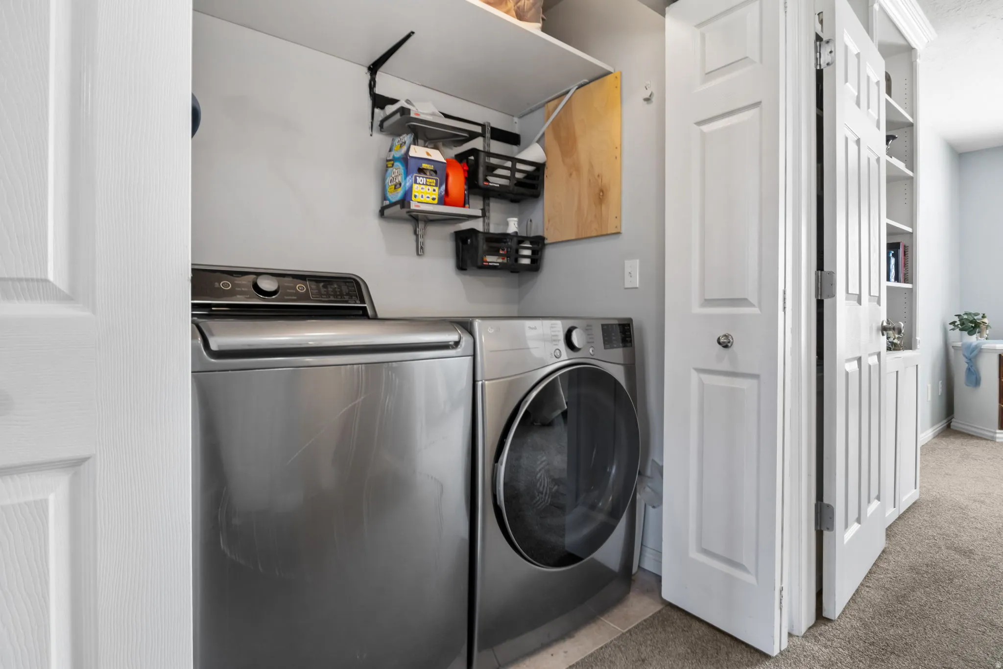 Laundry area with washer and dryer, light carpet, and light tile patterned floors