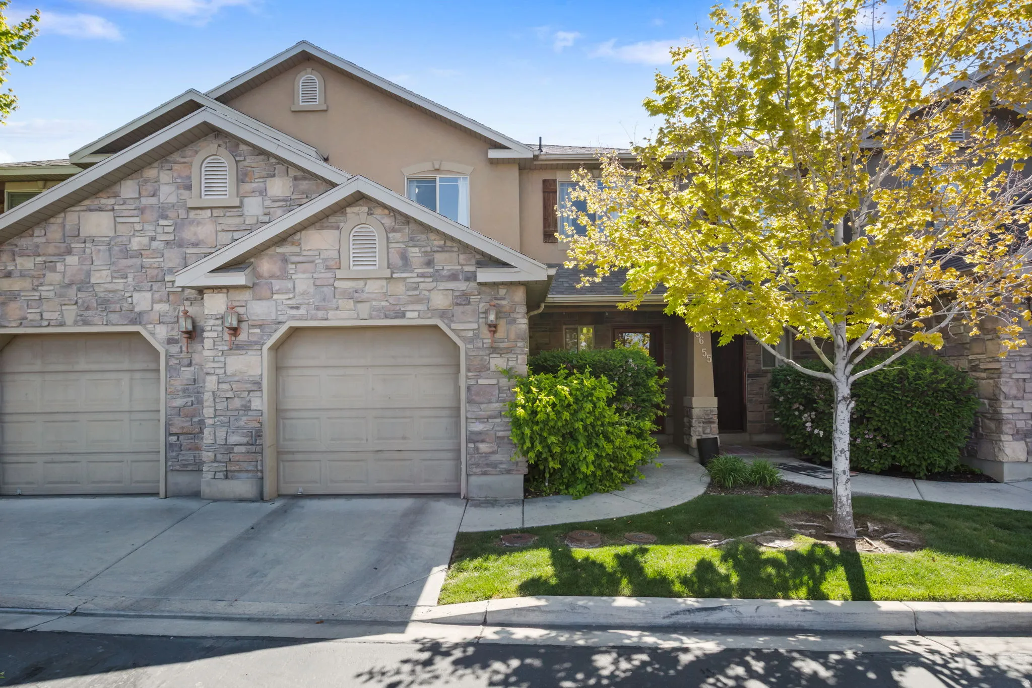 View of front of house with driveway, stucco siding, stone siding, and an attached garage