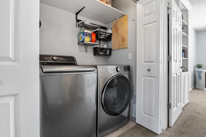 Laundry area with washer and dryer, light carpet, and light tile patterned floors