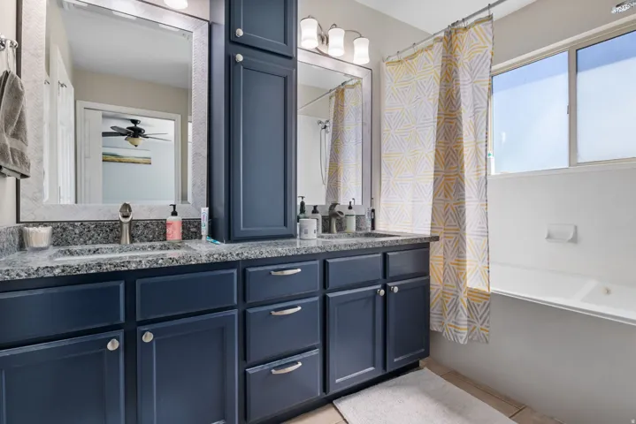 Bathroom featuring double vanity, shower / tub combo, and a ceiling fan