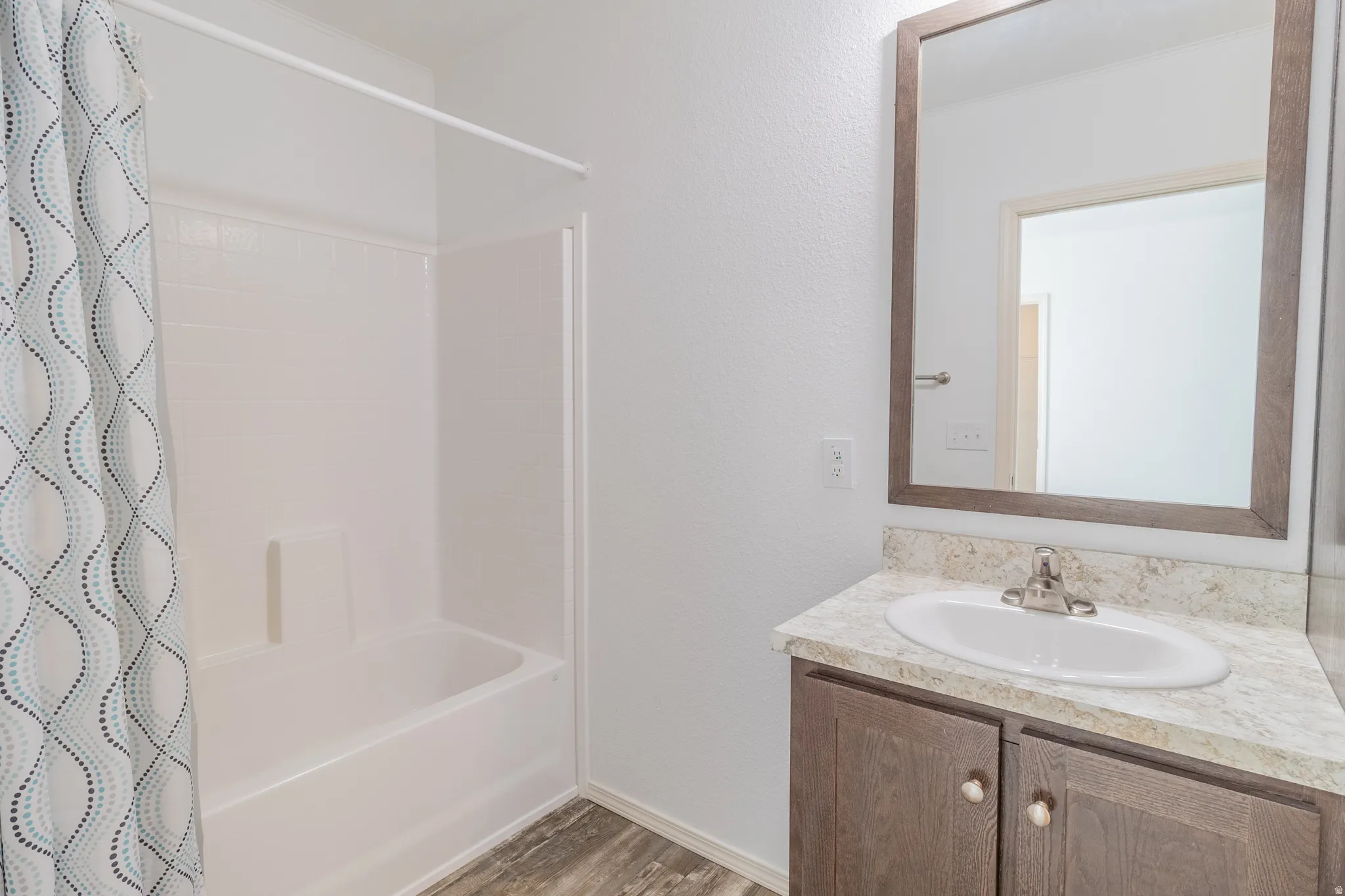 Bathroom with vanity, a textured wall, shower / tub combo with curtain, and light wood-style flooring