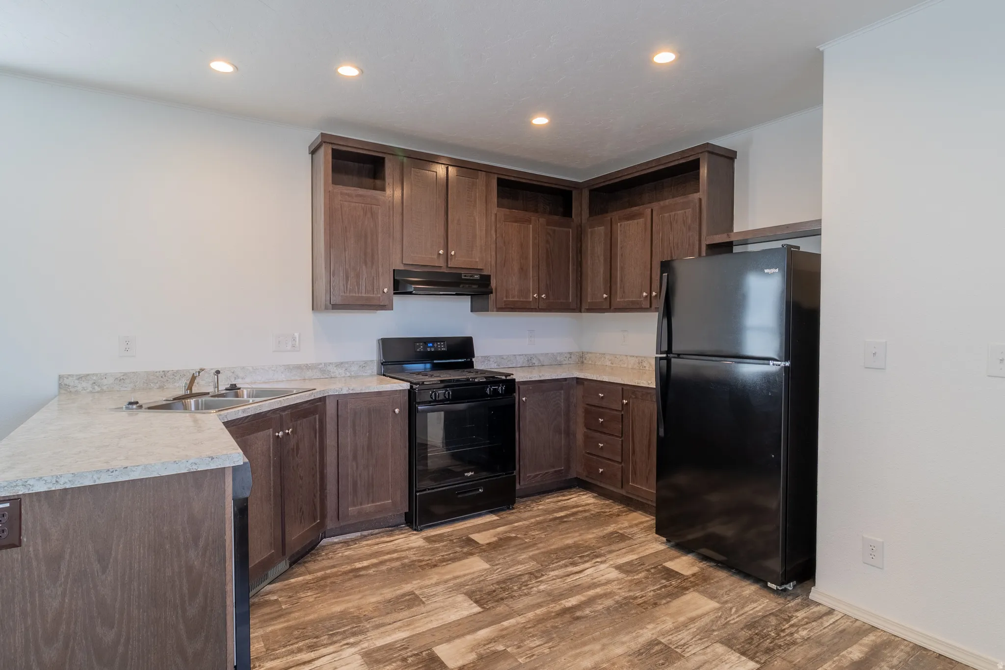 Kitchen with dark wood finish cabinets, black appliances, light countertops, light wood-style flooring, and a peninsula