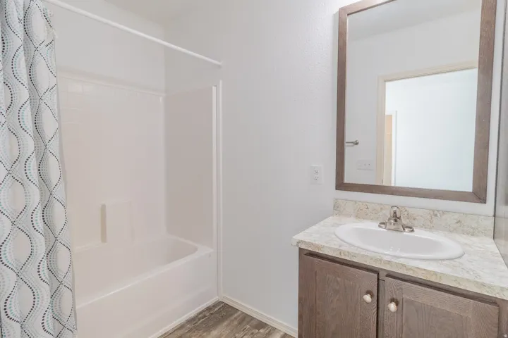 Bathroom with vanity, a textured wall, shower / tub combo with curtain, and light wood-style flooring