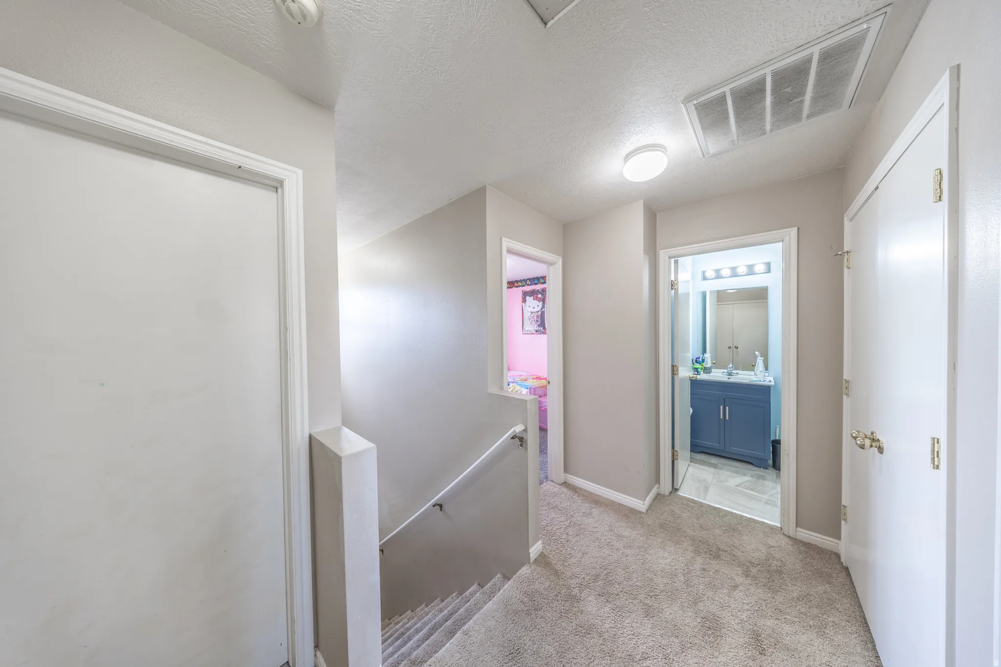 Hall featuring an upstairs landing, light carpet, and a textured ceiling