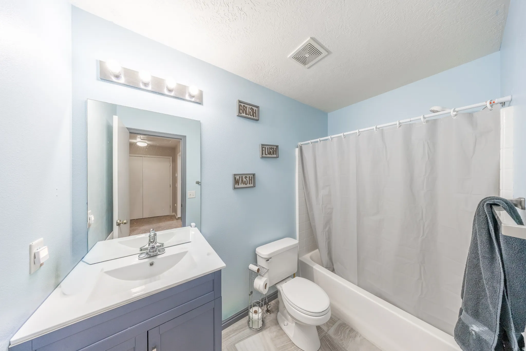 Bathroom featuring vanity, shower / bathtub combination with curtain, and a textured ceiling