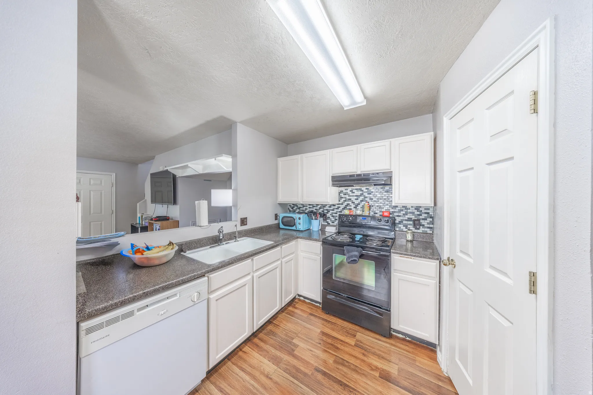 Kitchen featuring black electric range, white dishwasher, light wood-style floors, dark countertops, and decorative backsplash
