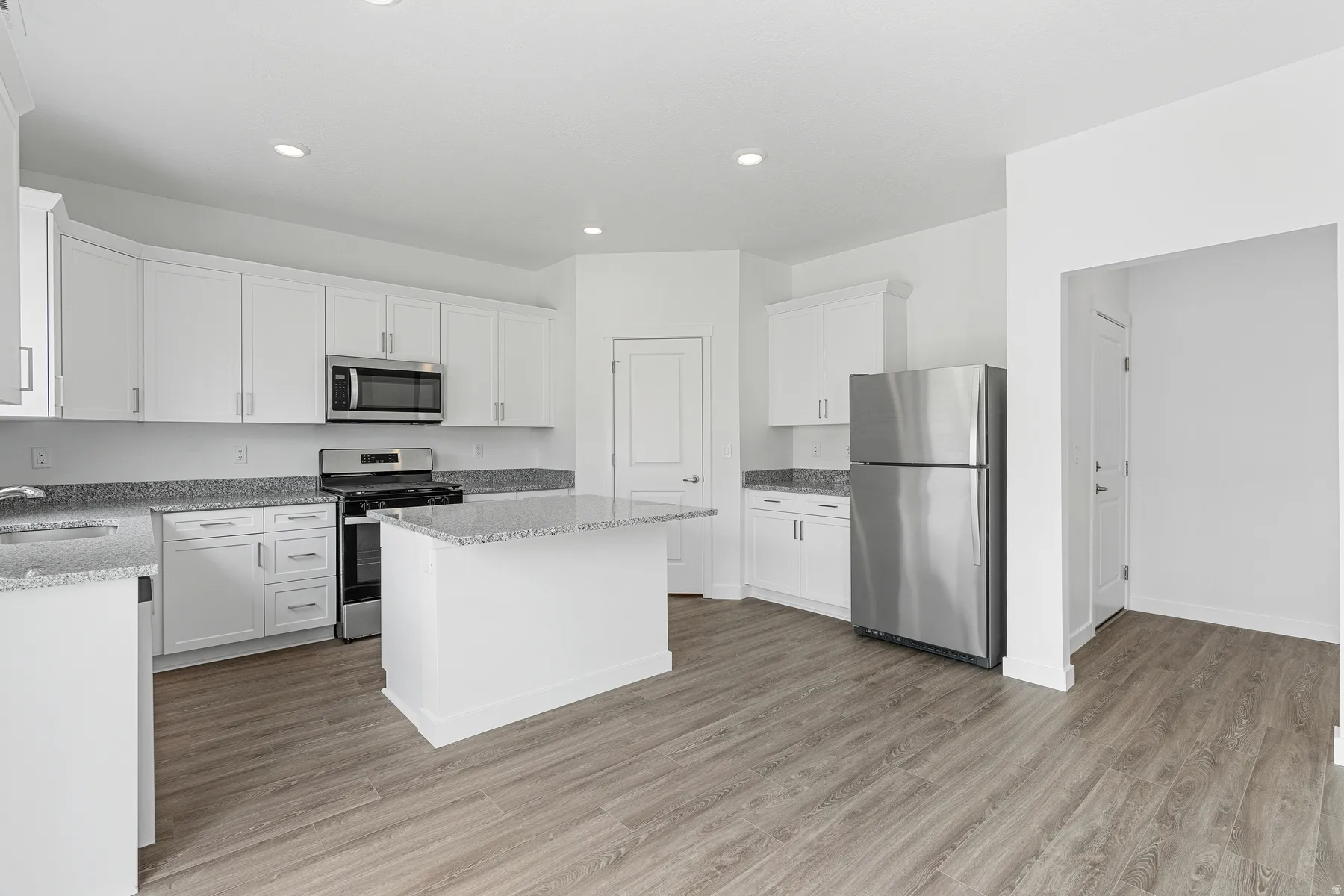 Kitchen featuring stainless steel appliances, light stone counters, light wood-type flooring, white cabinets, and a center island